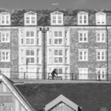 A cyclist is silhouetted against a row of apartments as they ride along above a lifeboat station